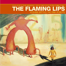 The Flaming Lips - Yoshimi Battles the Pink Robots album cover from Tandem Coffee Roasters shows a small figure facing a giant pink robot in a surreal landscape, inspired by dreamlike tracks such as Fight Test.