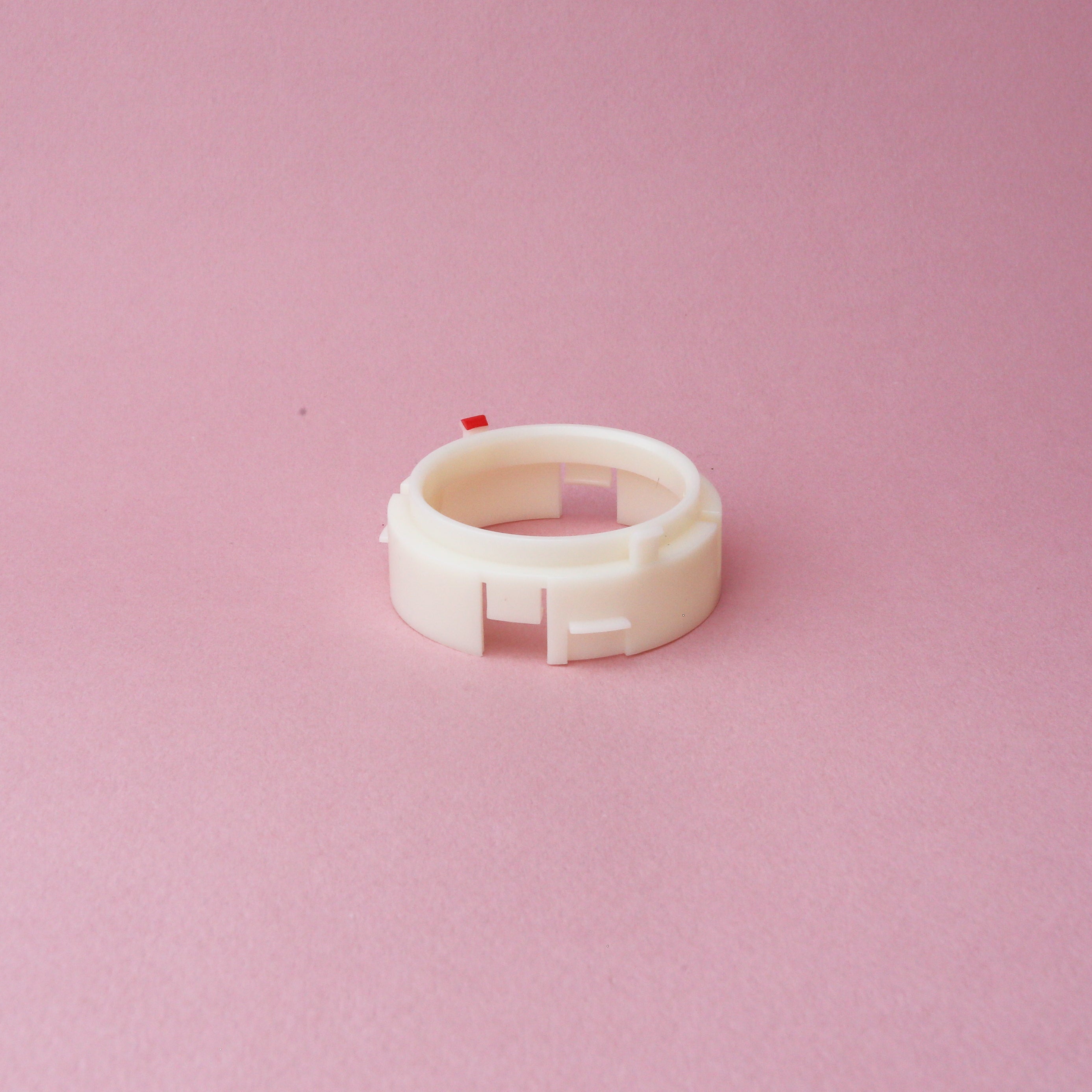 A white plastic Tandem Coffee Roasters Baratza Ring Burr Holder with small notches sits on a pink background.