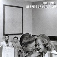 A black-and-white image captures a young couple sharing an intimate moment; the man leans in close to the woman, both smiling warmly. Two other people are seated in the background, also with smiles on their faces. The album title "John Prine - In Spite of Ourselves" is written in the upper right corner, suggesting an ensemble of heartfelt songs within. This evocative visual is brought to you by Tandem Coffee Roasters.