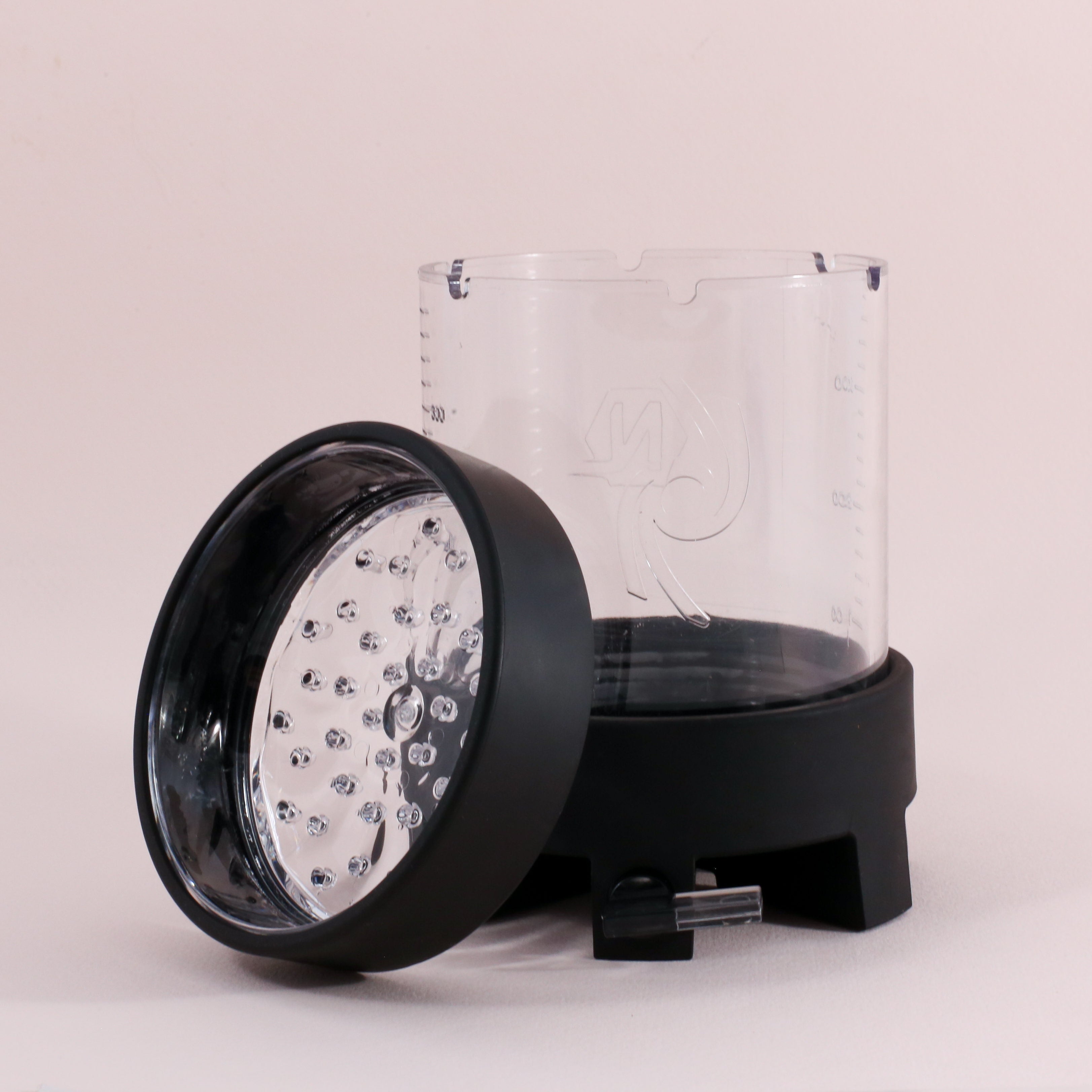The Tandem Coffee Roasters NextLevel Pulsar Brewer’s transparent pitcher with measurement markings stands upright, while its black and silver blade assembly lid with an adjustable flow valve rests tilted against it on a plain background.
