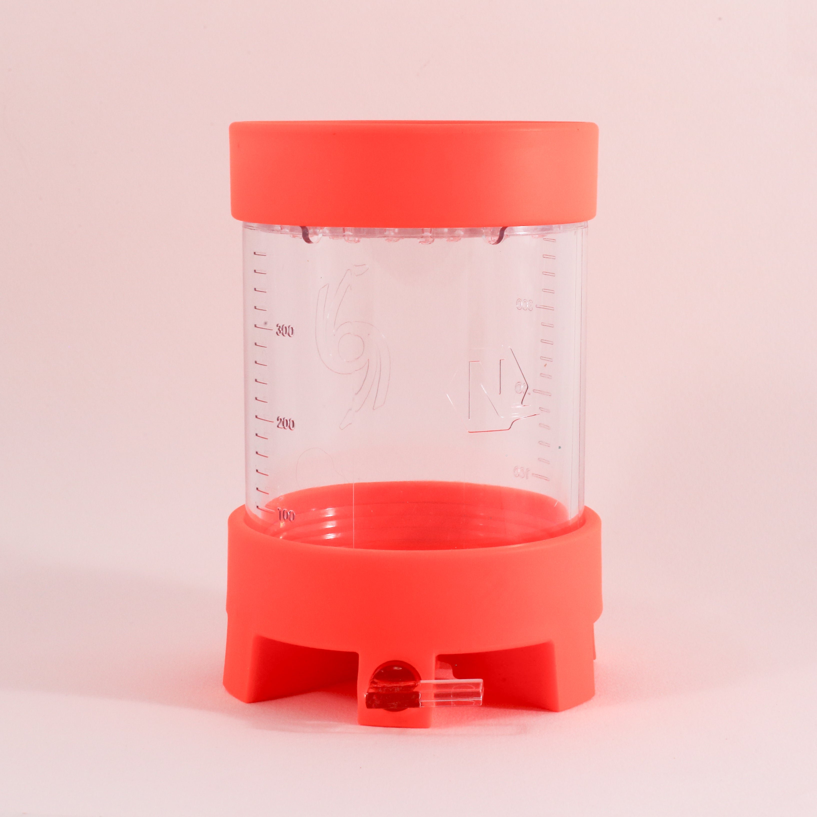The NextLevel Pulsar Brewer by Tandem Coffee Roasters is a transparent plastic container with red lids, vertical measurement markings, and an adjustable flow valve spout at the base, shown against a light pink background.