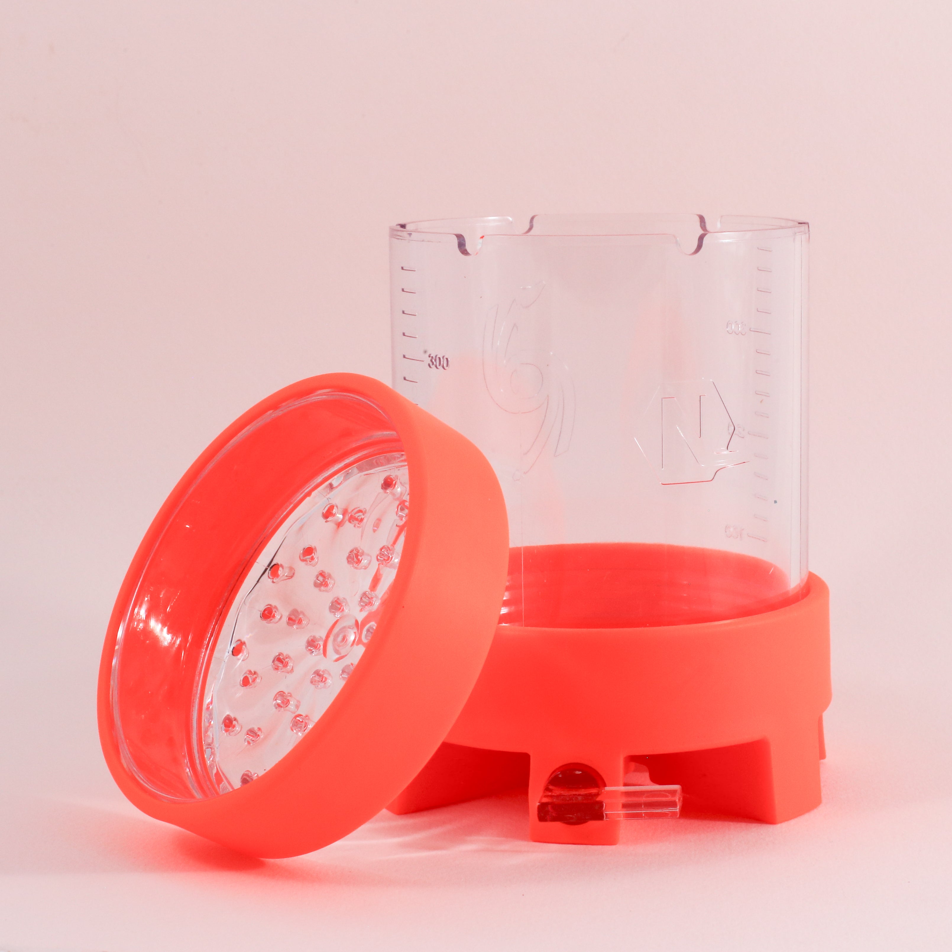 The NextLevel Pulsar Brewer by Tandem Coffee Roasters, featuring a clear container with measurement markings, an orange base, matching lid with textured surface, and adjustable flow valve, is set against a light pink background.