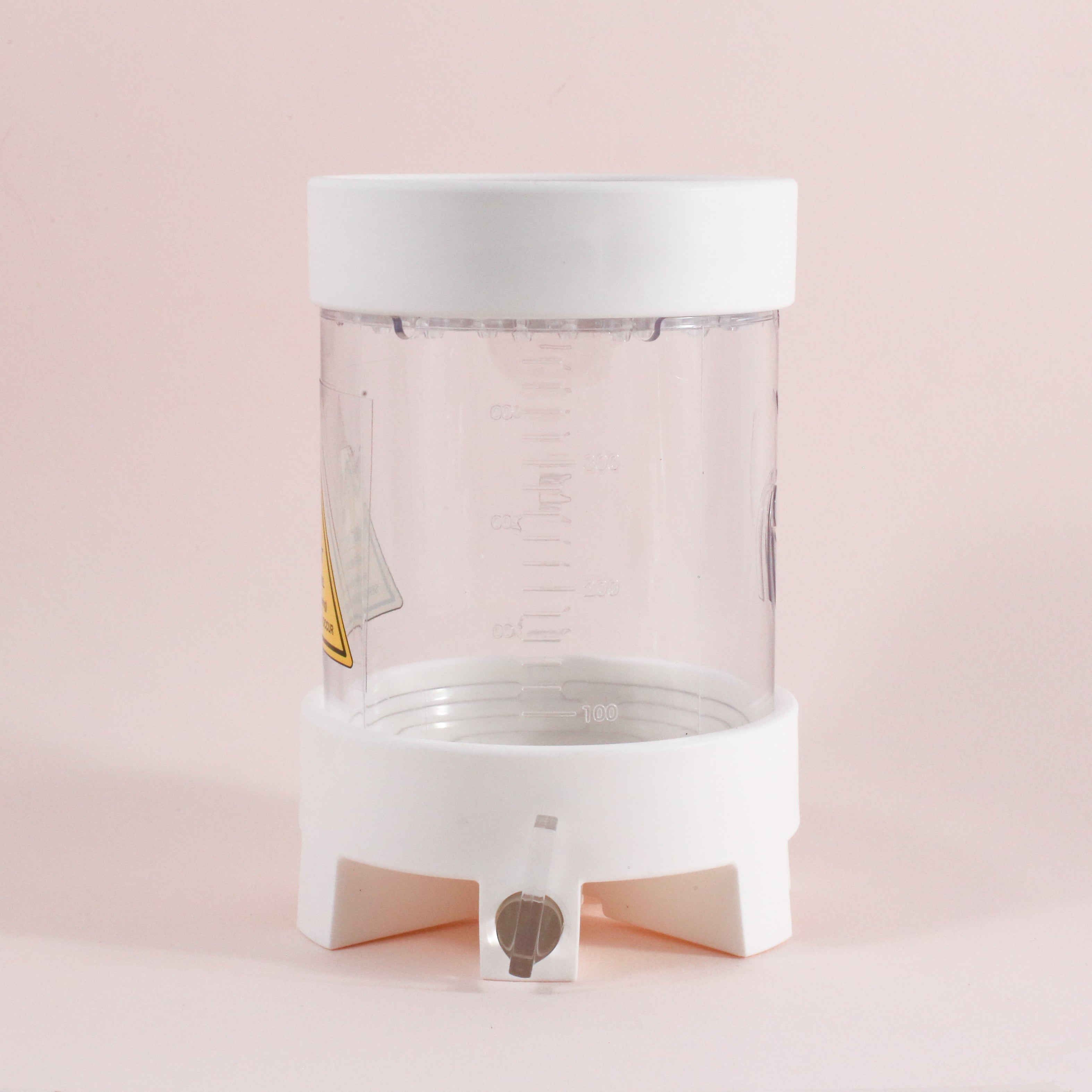 The NextLevel Pulsar Brewer by Tandem Coffee Roasters is a clear plastic container with a white lid and base, measurement markings, plus a small spout with adjustable flow valve, set against a light pink background.