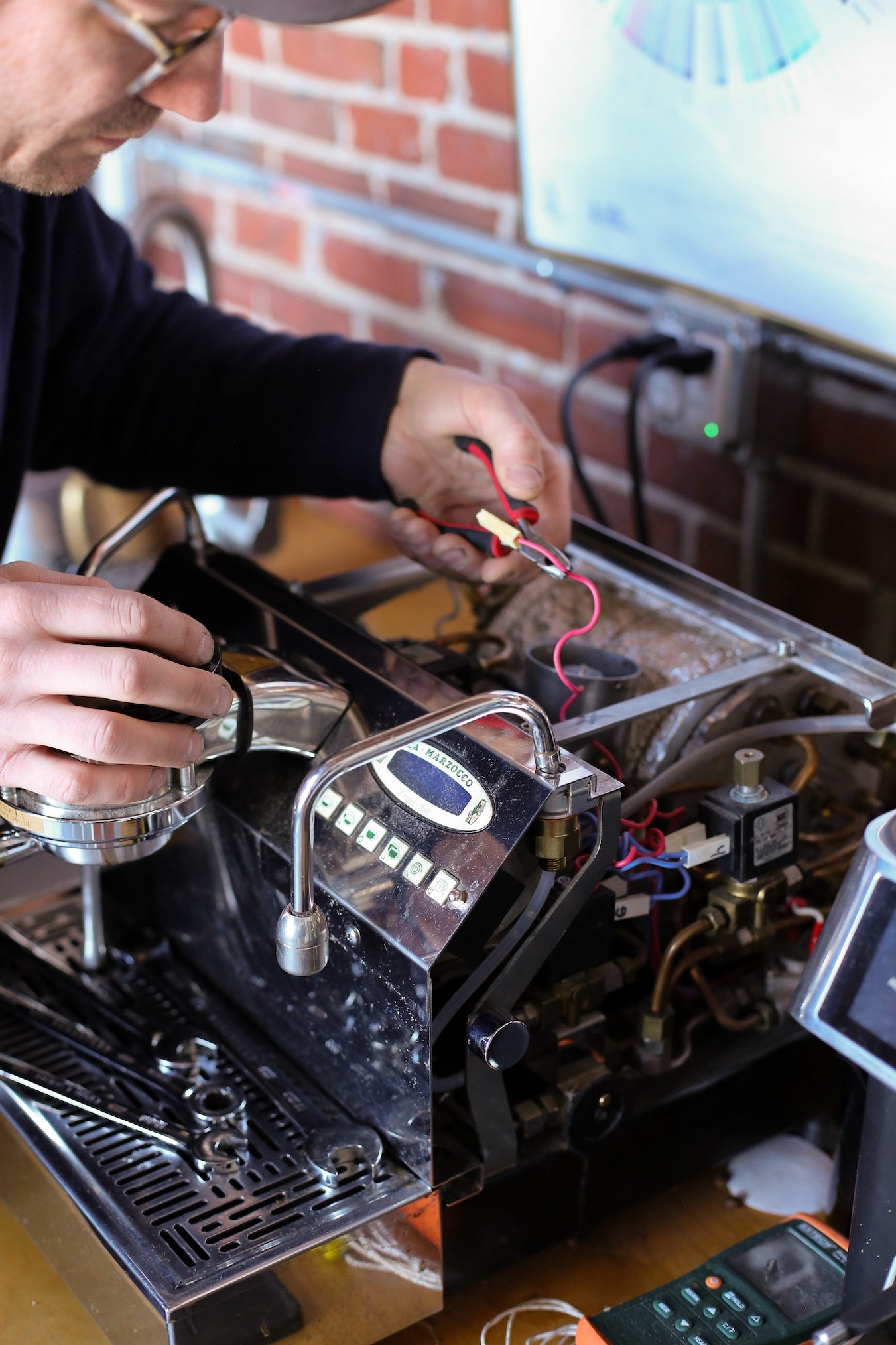 Person working on a coffee machine with a brick wall background