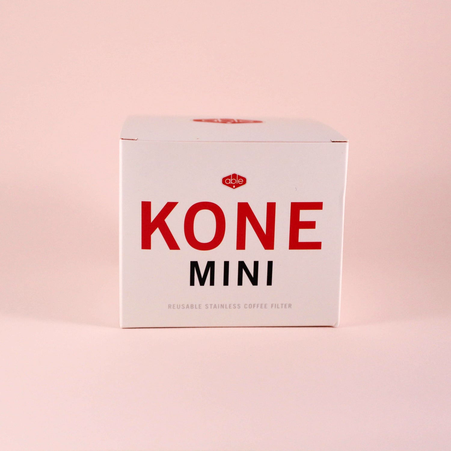 A white box with bold red text reading "Tandem Coffee Roasters Able Coffee Kone Mini" and smaller text stating "reusable stainless steel coffee filter" on a light pink background.