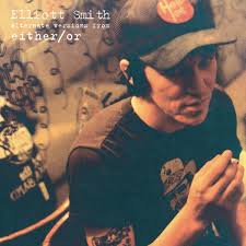 A man in a black cap and t-shirt with tattoos sits in a dim room. Above him, text reads: Tandem Coffee Roasters presents Elliot Smith - Either/Or alternate versions, including "Between the Bars," against patterned wallpaper and soft lighting.