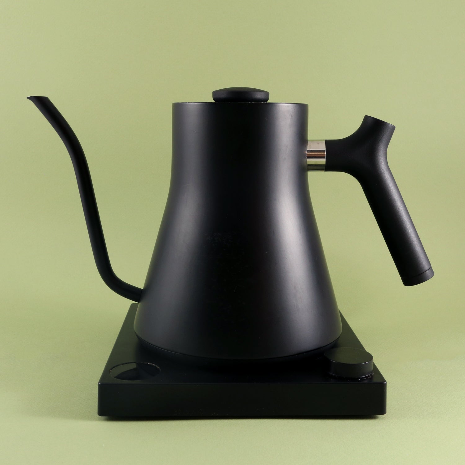 A Tandem Fellow Stagg EKG Pro Electric Kettle | Studio Edition in matte black with precision temperature control rests on a rectangular black base against a plain light green background.